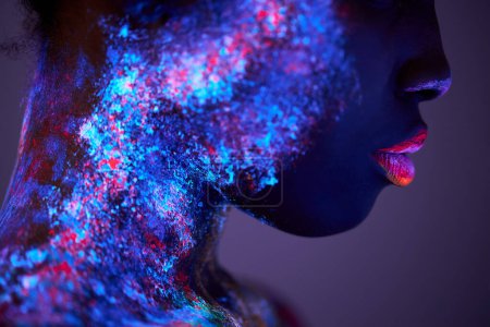 Foto de Body art glowing in ultraviolet light, close-up face of black woman with big lips, fluorescent body art isolated on purple studio background. futurustic, fashion, people, models concept - Imagen libre de derechos