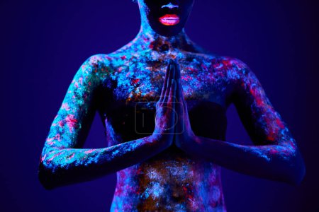 Téléchargez les photos : Fashion model woman in neon light, model with fluorescent make-up in prayer position, Art design of female posing in UV, colorful make up. Isolated on dark blue background. portrait close-up - en image libre de droit