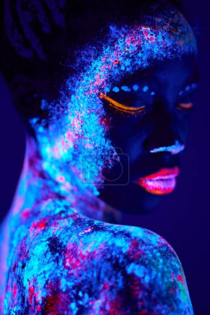 Photo for Beautiful black fashion woman in neon UF light. attractive young model with fluorescent creative psychedelic make-up, body-art. shoot from back, side view. art, fashion, lifestyle, people concept - Royalty Free Image