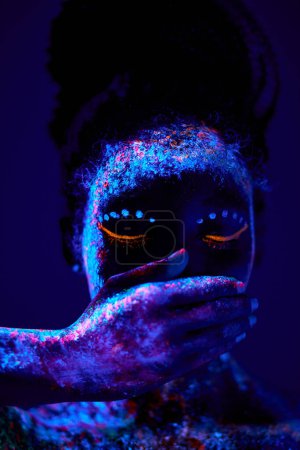 Foto de Beautiful black woman with creative fluorescent prints paintings on skin, on body, close mouth. cosmic art on body. neon lights, ultra-violet rays, luminescence, silence, beauty concept - Imagen libre de derechos