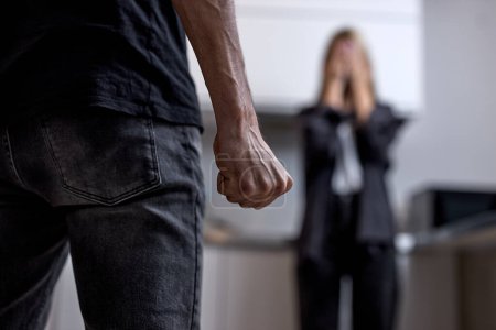 Photo for Aggressive Angry Husband Going To Beat Unhappy Crying Wife Standing In Background. Family Conflicts And Quarrels, Married Life With Abuser. Domestic Violence Concept. Focus On Male Fist - Royalty Free Image