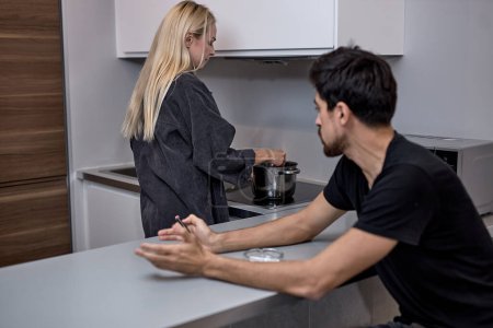Foto de Adult man and woman are arguing in kitchen at home. Angry woman is ignoring sad husband. Quarrel in Young Family. Divorce Concept. Upset Husband. Relationship between People Concept. - Imagen libre de derechos