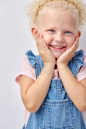 Foto de Wow. Closeup portrait of excited child touching cheeks, isolated over white studio wall, copyspace. curly blonde kid have fun, laughing, looking at side, posing. joy, fun, children emotions - Imagen libre de derechos