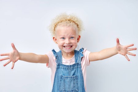 Photo for Excited expressive emotional blonde girl stretching arms for hug, looking at camera. Blue eyed child girl with curly hair is kind and pleasant. Natural beauty, children human emotions concept - Royalty Free Image
