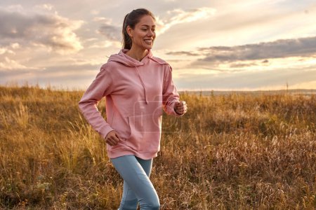 Photo for Woman in sportswear running in field at sunrise. Active rest on weekends. Traveling in nature. Caucasian european female enjoy sport, fitness outdoors. motivated healthy lady in the morning - Royalty Free Image