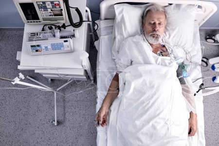 Photo for Top view on mature caucasian man has blood transfusion in hospital, patient with tube in mouth. ill male 60-70 years old suffering from coronavirus, covid-19. man lying on bed in private room - Royalty Free Image