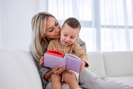 Téléchargez les photos : Adorable caucasian cute little boy listening mother, reading funny story or fairy tales. young beautiful woman having rest, spending leisure time, sitting on sofa with son, leisure time. in cozy room - en image libre de droit