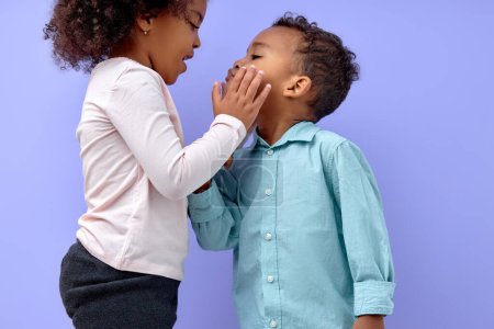 Photo for Two cheerful black american siblings, sister kissing her brother, isolated on purple background. portrait of cute kids in casual clothes. Boy and girl feeling love to each other. - Royalty Free Image