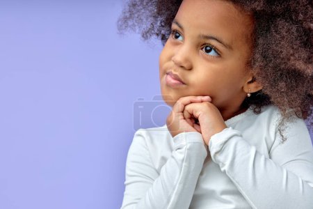 Téléchargez les photos : Thoughtful little black girl six years old daughter look away on copy space thinking isolated on purple background, funny kid dreaming about something, looking pretty and charming - en image libre de droit