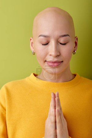 Foto de Beautiful young caucasian bald hairless woman praying, keeping hands together, wearing casual clothes standing isolated over green background, asking for something, thanks God concept - Imagen libre de derechos