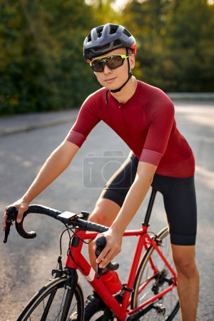 Téléchargez les photos : Fit man ride on bike on road. Sport and active life concept sunset time. Athlete riding on bicycle in park at summer season. Handsome guy in sportive outfit and protective helmet, eyeglasses - en image libre de droit