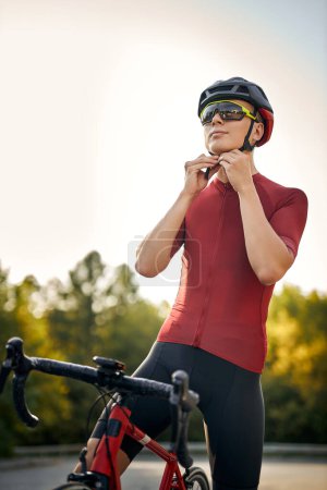 Téléchargez les photos : Young caucasian male is wearing helmet for riding a bike outdoors, looking at side. handsome sportive athlete guy in red t-shirt is engaged in sport, riding bicycle as profession. healthy lifestyle - en image libre de droit