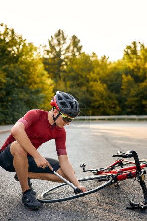 Foto de It needs to be fixed. concentrated young european man in sportive wear and helmet using tool while repairing bike outdoors, preparing to ride a bike, engaged in healthy lifestyle, hobby concept - Imagen libre de derechos
