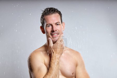 Téléchargez les photos : Satisfied american guy getting shower alone, posing at camera, indoors. handsome male with naked muscular torso enjoy freshness, touching chin after shaving beard, foam advertisement - en image libre de droit