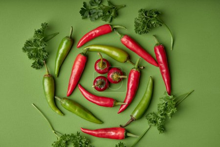 Foto de Spicy red hot chilli pepper and greenery on green background. Copy space for text. Top view or flat lay. Group of red peppers isolated on green background - Imagen libre de derechos