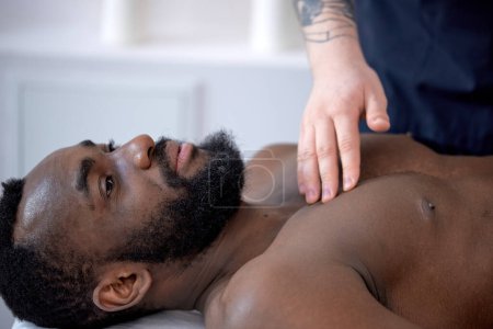 Téléchargez les photos : Cropped acupuncturist doctor preparing clint for acupuncture at special points on chest. Acupuncture is alternative medicine. handsome black bearded guy lying on couch in clinic hospital - en image libre de droit