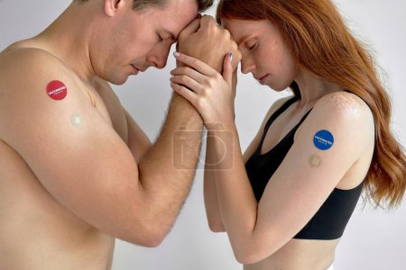 Foto de Young caucasian couple showing COVID-19 vaccine on arm in concept of global coronavirus vaccination program to vaccinate citizen. portrait of shirtless guy and redhead female holding hands together. - Imagen libre de derechos