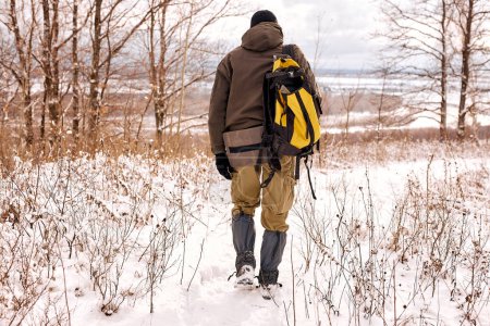 Photo for Rear view on unrecognizable man travelling with backpack. Winter hike in forest. Tourist on walk in winter in forest, nature. bushcraft, hunting, travel, hike concept. view from back - Royalty Free Image