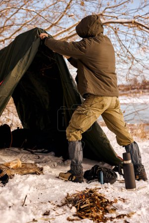 Photo for Rear view on male hiker setting up tent in forest, pitching in forest clearing, getting ready for camping. young traveller in warm clothes, alone. bushcraft, travel, adventure, hiking, wanderlust - Royalty Free Image