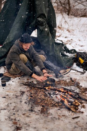 Téléchargez les photos : Happy Man warming hands on bonfire in nature in cold season, winter. travel lifestyle photo. adventure active vacations outdoor. Extreme camping. in snowy frozen forest alone, calm and pacified - en image libre de droit