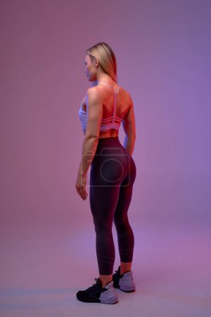 Téléchargez les photos : Musclé corps féminin sexy, sportive dans des vêtements de sport de luxe élégant. fond violet isolé. - en image libre de droit