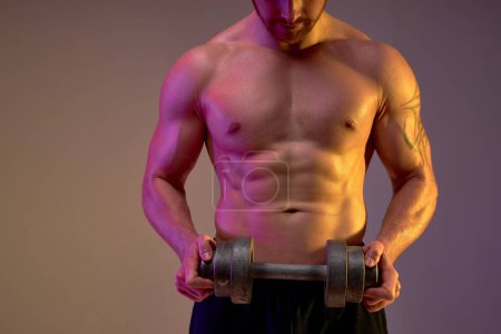 Photo for Close up cropped shot of males body with perfect six-packs, abs with dumbbell, tired sportsman takes break,isolated brown background - Royalty Free Image