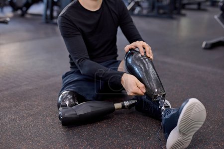 Téléchargez les photos : Gars en vêtements de sport élégant enlever sa jambe prothétique après l'entraînement, près de la photo recadrée. se concentrer sur la jambe artificielle - en image libre de droit