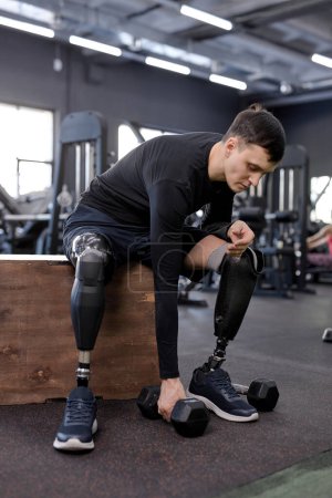 Photo for Young ambitious man going to do exercises with dumbbells, sportsman is stretching to take dumbbell. full length side view shot, weightlifting, powerlifting - Royalty Free Image
