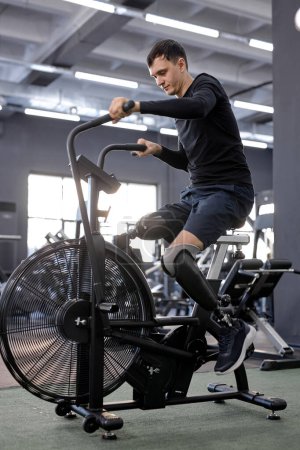 Téléchargez les photos : Ambitieux gars en vélo stationnaire à la salle de gym. vue latérale, santé et soins du corps. bien-être. entraînement cardio - en image libre de droit