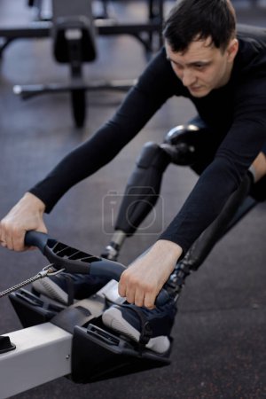 Photo for Motivated sportsman with artificial legs limb working out in gym on rowing machine, lifestyle spare time, health and body care, cropped photo. focus on legs - Royalty Free Image