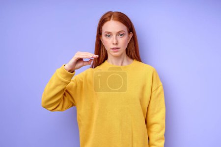 Foto de Hermosa mujer pelirroja confiada seria en suéter amarillo demostrando letra D símbolo de lenguaje de signos para sordos humanos con fondo azul. aislado - Imagen libre de derechos