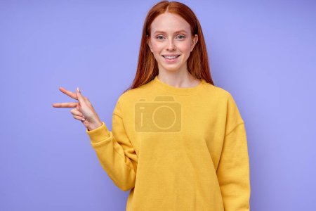 Téléchargez les photos : Belle femme rousse heureuse en pull élégant jaune démontrant la lettre K symbole de langue des signes pour les sourds humains avec fond bleu. portrait isolé en gros plan - en image libre de droit