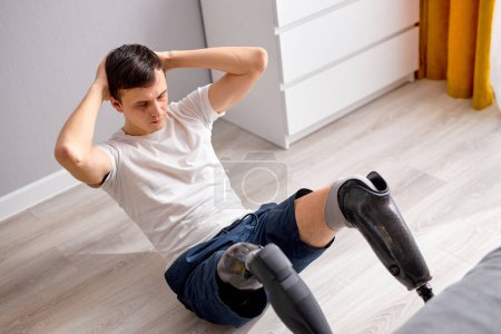Photo for Amputated handicapped man. young Caucasian guy with leg prosthesis training at home, engaged in sport. body positivity and self esteem concept. Disabled sport and overcoming, wellness concept. - Royalty Free Image