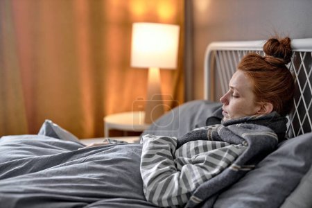 Téléchargez les photos : Fatigué épuisé rousse femme au repos, pâle pauvre fille qui dort, ronflement concept de surmenage, femme malsaine couché à la maison à la lampe de nuit en arrière-plan de photo vue de près portrait - en image libre de droit