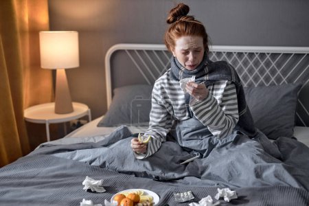 Photo for 25s woman with cold blowing runny nose. female sneezing in tissue in bedroom. Sick young woman under blanket in domestic interior. Woman sick in bed with temperature high fever, at home - Royalty Free Image