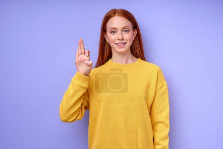 Foto de Joven dama con el pelo largo y liso vestido con suéter elegante amarillo mantener la mano levantada mientras muestra f alfabeto sordo, primer plano retrato aislado fondo azul - Imagen libre de derechos