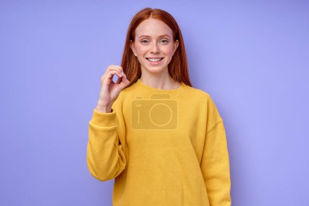 Photo for Beautiful redhead happy cheerful girl, teacher showing letter O on blue background. Sign language alphabet. free education for deaf children - Royalty Free Image