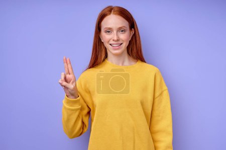 Foto de Letra U ortografía por las niñas mano en American Sign Language ASL sobre fondo azul, primer plano retrato, feliz sonriente mujer caucásica demostrando la letra U símbolo de lenguaje de signos para sordos humanos - Imagen libre de derechos