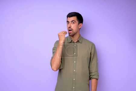 Téléchargez les photos : Jeune homme sourd affamé en chemise verte élégante montrant geste alimentaire. gars veut manger de près portrait isolé fond bleu - en image libre de droit