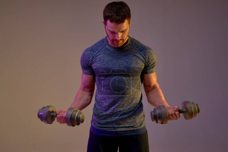 Photo for Young ambitious man burning Calories, Fat, and Controlling Diabetes. close up photo. sportsman with dumbbells looking down. guy doing exercises for biceps. isolated brown background - Royalty Free Image