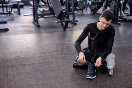 Photo for Young male athlete putting on sneakers on his artificial leg, disabled guy ties his shoes. close up photo. copy space - Royalty Free Image