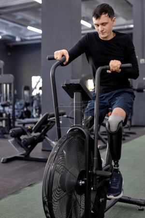 Foto de Hombre cansado y agotado con piernas artificiales haciendo ejercicio en bicicleta, cansancio, resistencia - Imagen libre de derechos