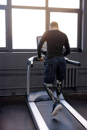 Photo for Back shot of man with artificial legs running on treadmills at gym, free time, spare time, daily routine wellness. rehabilitation center, practicing. Active man with handicap. - Royalty Free Image