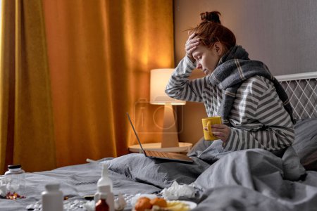 Photo for Redhead woman having cough, sneezing, feeling sick while working online from home, freelance during covid-19, coronavirus, omicron. female with headache drinking hot tea to lower the temperature - Royalty Free Image