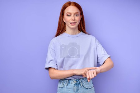 Photo for Attractive smiling ginger girl asking time, touching her arm, wrist, what time is it now close up portrait isolated blue background it is time - Royalty Free Image
