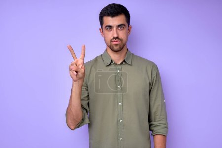 Foto de Serio hombre guapo mostrando letra V v con los dedos .the alfabeto en el lenguaje de señas americano ASL. retrato de primer plano de fondo azul aislado - Imagen libre de derechos