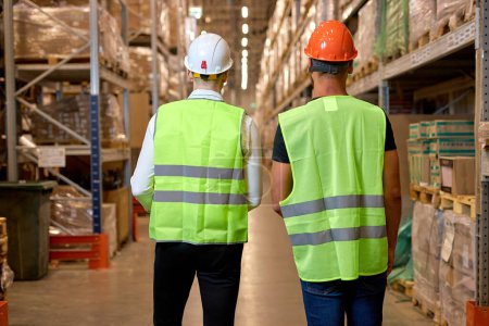 Photo for Rear view on Manager and staff talking, discussing while walking in warehouse. caucasian people in factory with safety helmet, vest. Concept for industry, job, meeting, work training and teamwork. - Royalty Free Image