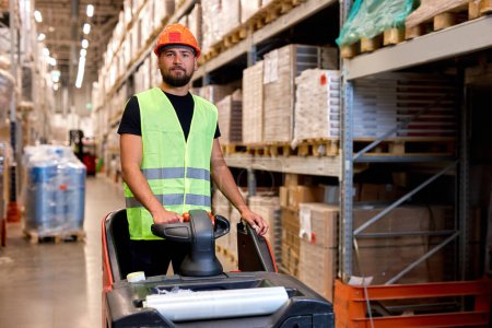 Photo for Forklift driver in warehouse. freight transport, Warehouse industrial delivery shipment, young caucasian male pushing transport equipment, dressed in green uniform vest and safety helmet - Royalty Free Image