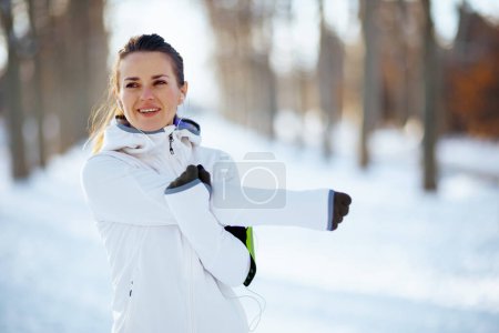 Foto de Mujer en forma feliz chaqueta blanca que se extiende fuera en el parque de la ciudad en invierno. - Imagen libre de derechos