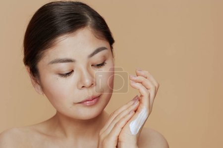 Téléchargez les photos : Moderne asiatique femelle avec crème pour les mains sur fond beige. - en image libre de droit